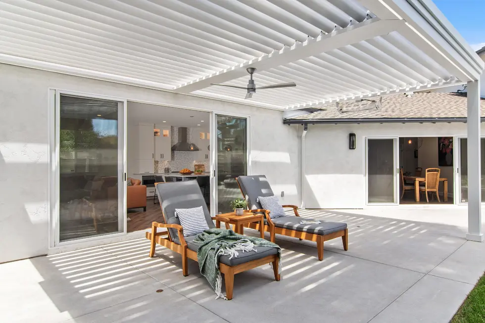 White louvered pergola covering two lounge chairs on a sunny patio with sliding doors leading into the home