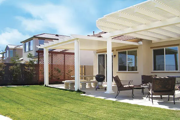 Stone column-supported pergola in a landscaped backyard with an outdoor dining table and surrounding plants.