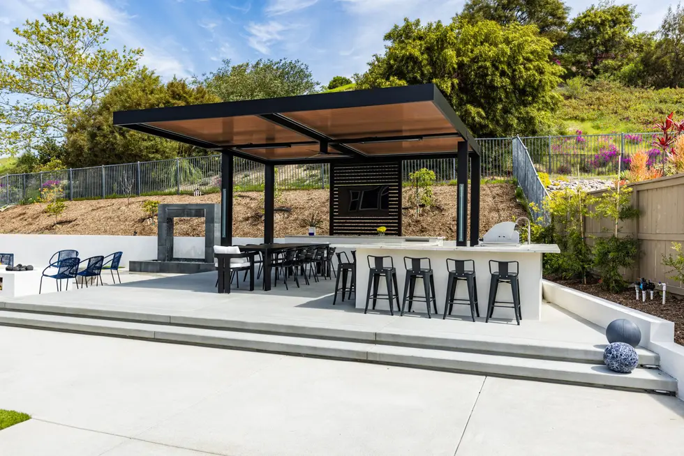 Modern outdoor bar and grill area with long counter and high stools under a sleek black pergola