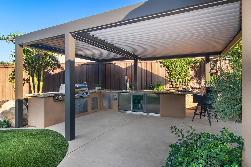 Covered outdoor kitchen with built-in grill, sink, and bar under a sleek aluminum pergola