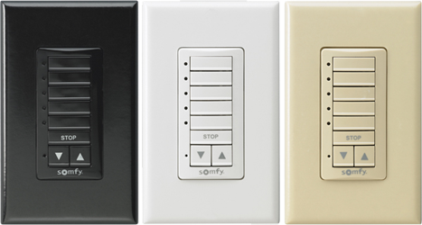 Three wall-mounted Somfy control switches in black, white, and beige, each with directional and stop buttons.