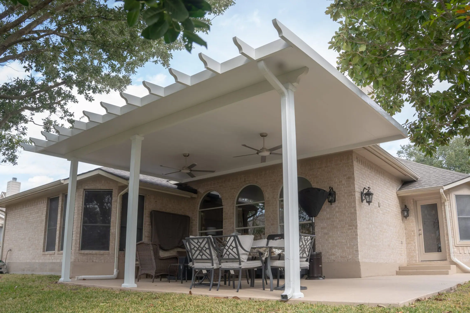 Modern backyard patio with black pergola, white ceiling fans, and a long dining table with blue chairs